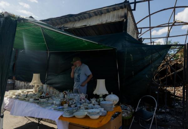 Vadym vend des objets sur son étal du marché aux puces de Potchaïna endommagé par une frappe russe, le 9 août 2026 à Kiev, en Ukraine