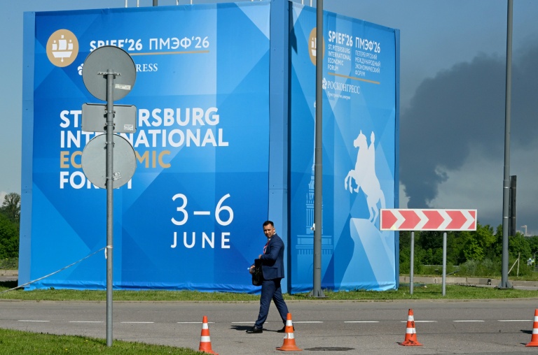 Un homme passe devant des affiches du Forum économique international de Saint-Pétersbourg alors que de la fumée s'élève en arrière-plan après des frappes de drones ukrainiens, le 3 juin 2026 en Russie
