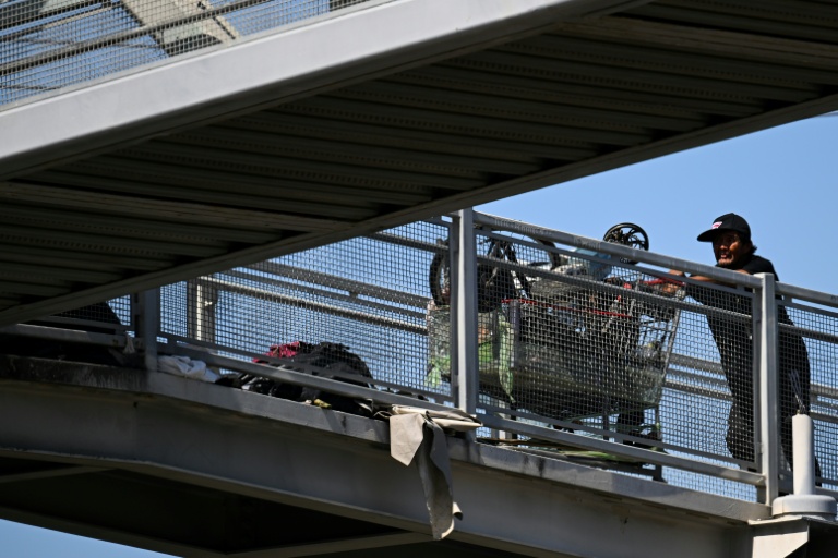 Un sans-abri pousse un chariot rempli d'affaires, sur un pont près d'un campement de SDF, à Los Angeles, le 1er juin 2026