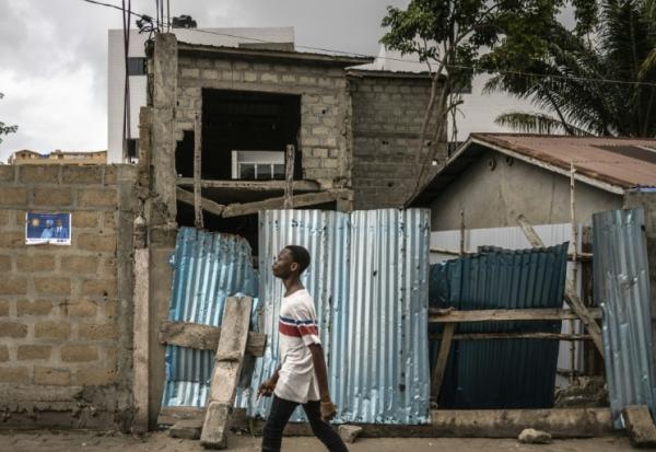 Un jeune homme marche dans un quartier de Cotonou le 9 avril 2026, près d'une affiche électorale placardée au mur 