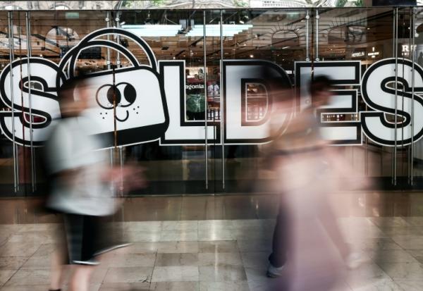 Des passants marchent à proximité de l'entrée d'un centre commercial annonçant les soldes, le 25 juin 2025 à Paris