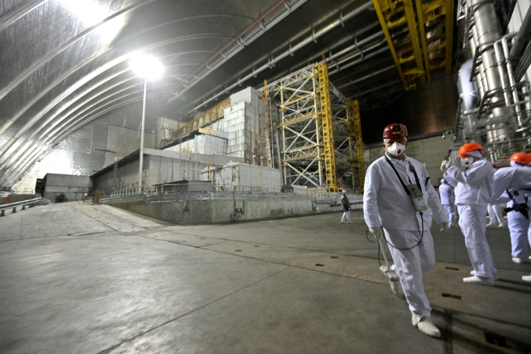 Des employés et des visiteurs marchent devant le sarcophage recouvrant le réacteur 4 détruit, sous la nouvelle enceinte de confinement dans la centrale nucléaire de Tchernobyl, le 24 avril 2026