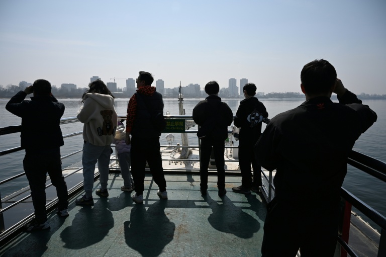 Des touristes observent la ville nord-coréenne de Sinuiju (arrière-plan) depuis un bateau touristique sur le fleuve Yalu, dans la ville frontalière de Dandong, dans le nord-est de la Chine, le 26 mars 2026