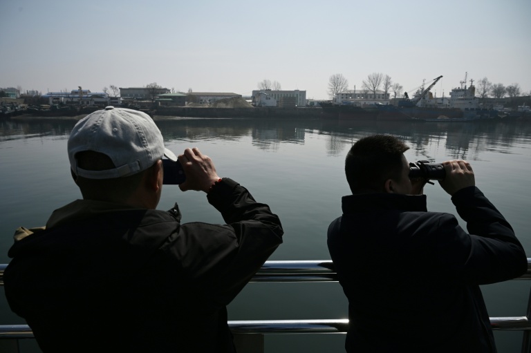Des touristes observent la ville nord-coréenne de Sinuiju depuis un bateau touristique sur le fleuve Yalu, dans la ville frontalière de Dandong, dans le nord-est de la Chine, le 26 mars 2026