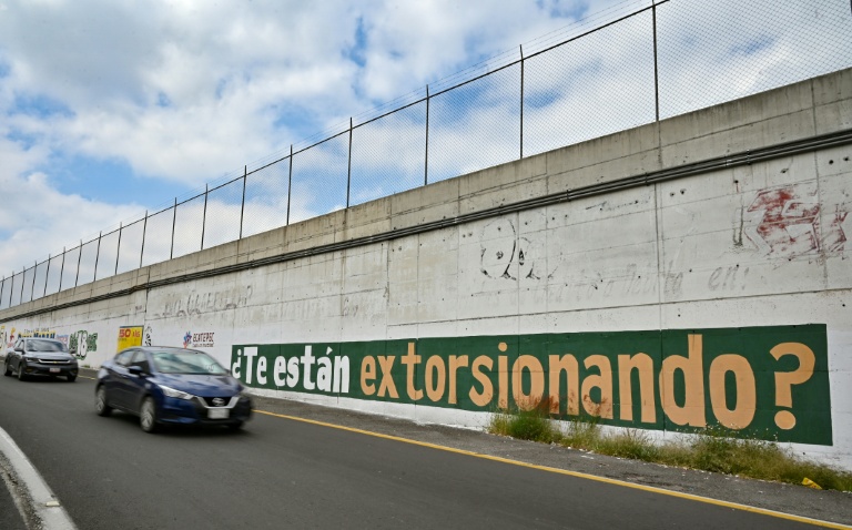 Des automobilistes passent devant un message du gouvernement peint sur un mur exhortant les habitants à signaler les cas d'extorsion à Ecatepec, dans l'Etat de Mexico, le 2 octobre 2025