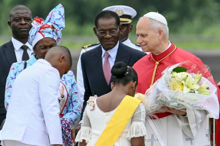 Le pape Léon XIV (à droite) reçoit des fleurs d'enfants alors qu'il est accueilli par le président de Guinée équatoriale Teodoro Obiang Nguema Mbasogo (au centre) à son arrivée à l'aéroport international de Malabo à Malabo le neuvième jour d'un voyage apostolique de 11 jours en Afrique, le 21 avril 2026.