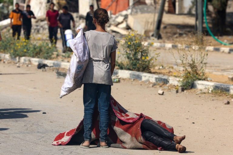 Une enfant palestinienne se tient devant le corps d'une personne tuée en venant chercher des vivres dans un site de distribution de la Fondation humanitaire de Gaza (GHF) soutenue par Israël et les Etats-Unis, dans le centre de la bande de Gaza, le 4 août 2025