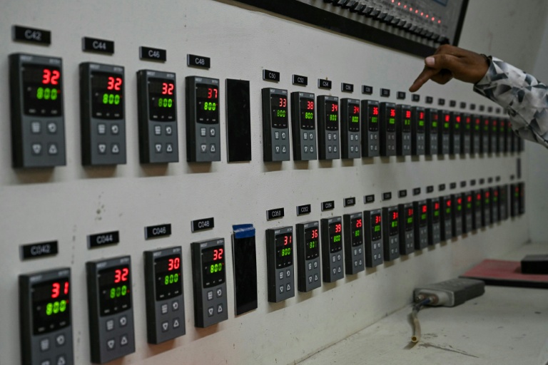 Un superviseur montre un panneau de contrôle affichant les relevés de température d'un four à propane hors service dans une usine de fabrication de carreaux de céramique, qui reste fermée, le 26 mars 2026 à Morbi, en Inde