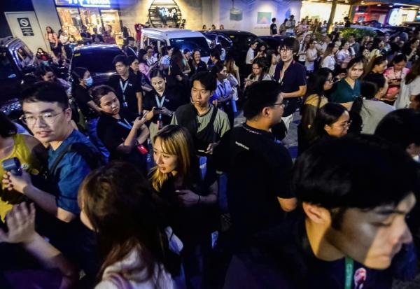 Les employés du centre d'appels surfent sur leurs téléphones portables alors qu'ils se rassemblent devant leur immeuble de bureaux après les secousses du tremblement de terre à Cebu, dans le centre des Philippines, le 30 septembre 2025