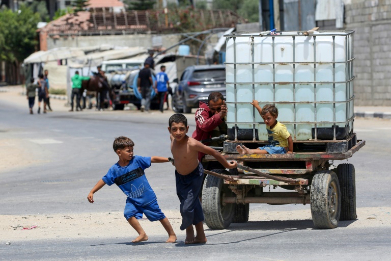 Un homme et des enfants poussent un chariot transportant un réservoir d'eau à Bureij dans le centre de la bande de Gaza, le 17 août 2025