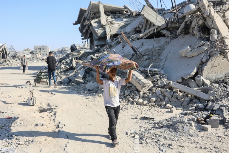Un garçon palestinien transporte des affaires au milieu des décombres de bâtiments détruits dans un quartier de Gaza-ville, le 27 octobre 2025