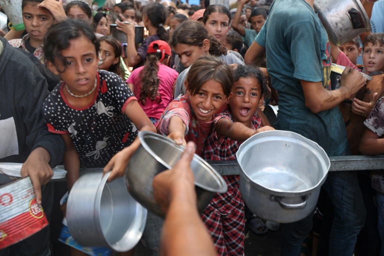 De jeunes palestiniens attendent de recevoir des repas cuisinés dans le camp de réfugiés de Nousseirat, dans le centre de la bande de Gaza, le 18 août 2025