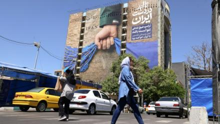 Des passants près d'un panneau d'affichage sur la façade d'un immeuble représentant le détroit d'Ormuz avec une inscription en persan disant "À jamais dans la main de l'Iran", place Vanak à Téhéran, le 25 mai 2026