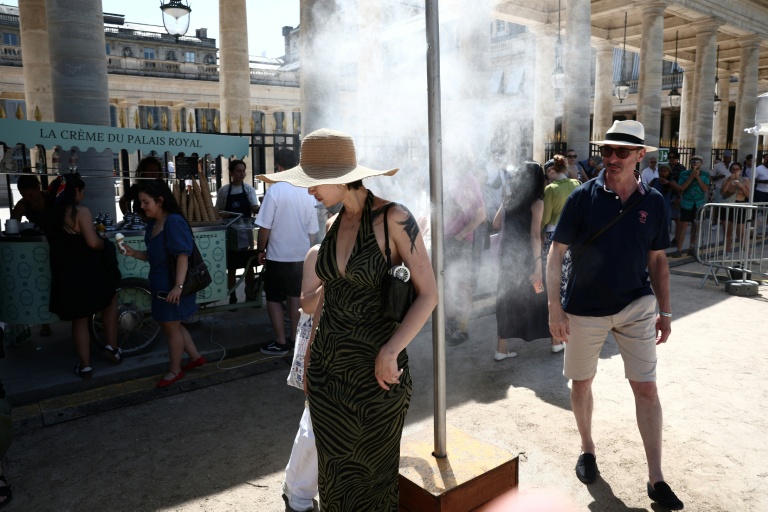Des piétons se rafraîchissent sous un brumisateur installé par la mairie de Paris pendant une vague de chaleur à Paris, le 21 juin 2026