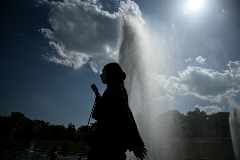 Une personne tient un éventail en passant devant une fontaine, le 22 juin 2026 à Paris