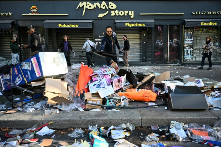 Un commerçant déblaie les débris devant sa boutique endommagée, au lendemain de manifestations nationales contre la vie chère, le 18 octobre 2026 à Paris