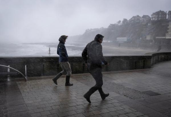 Des promeneurs pris dans les bourrasques de la tempête Austen sur le front de mer à Granville, dans la Manche, le 23 octobre 2026