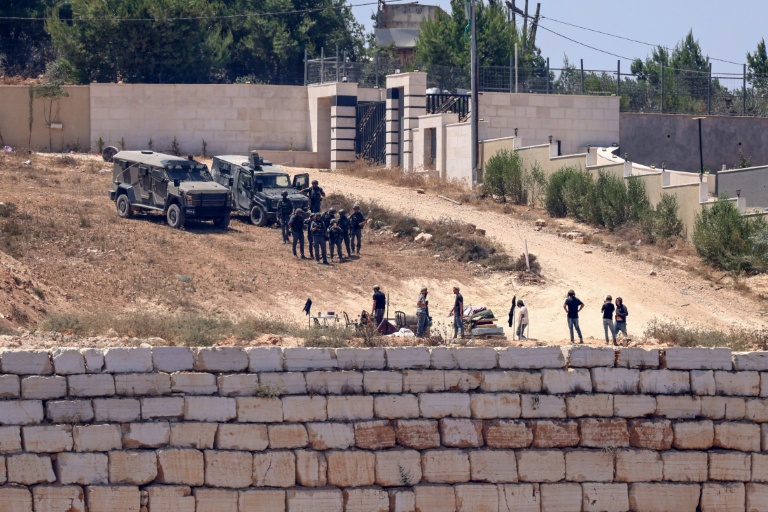 Des soldats israéliens (en haut) montent la garde aux côtés de colons devant des maisons palestiniennes dans le village de Qusra, au sud de Naplouse, en Cisjordanie occupée, le 12 août 2026