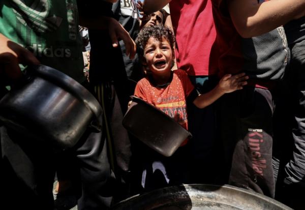 Un enfant pleure au milieu de Palestiniens qui attendent de recevoir un repas chaud distribué par une association caritative locale à Nousseirat, dans le centre de la bande de Gaza, le 24 mai 2025