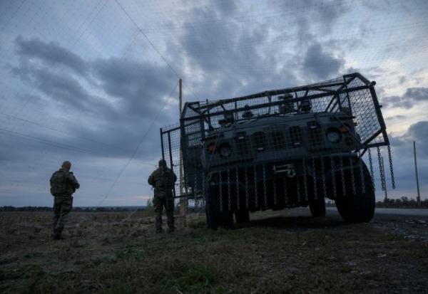 Des soldats ukrainiens devant un véhicule militaire blindé entouré d'une cage de protection contre les attaques de drones, sur une route près d'Oleksandrivka, le 6 octobre 2025