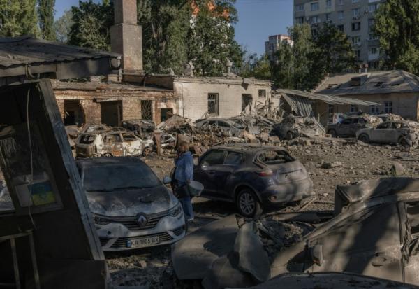Une femme se tient près de voitures détruites et de bâtiments endommagés après une frappe russe à Kiev, le 20 août 2026