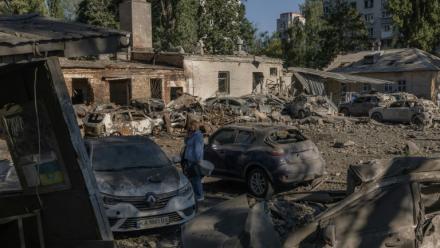 Une femme se tient près de voitures détruites et de bâtiments endommagés après une frappe russe à Kiev, le 20 août 2026