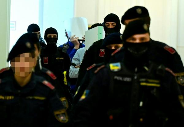 Deux accusés, escortés par des policiers, cachent leurs visages à leur arrivée à la salle d'audience du tribunal de Wiener Neustadt, en Autriche, le 28 avril 2026, pour un projet d'attentat lors d'un concert de Taylor Swift à Vienne