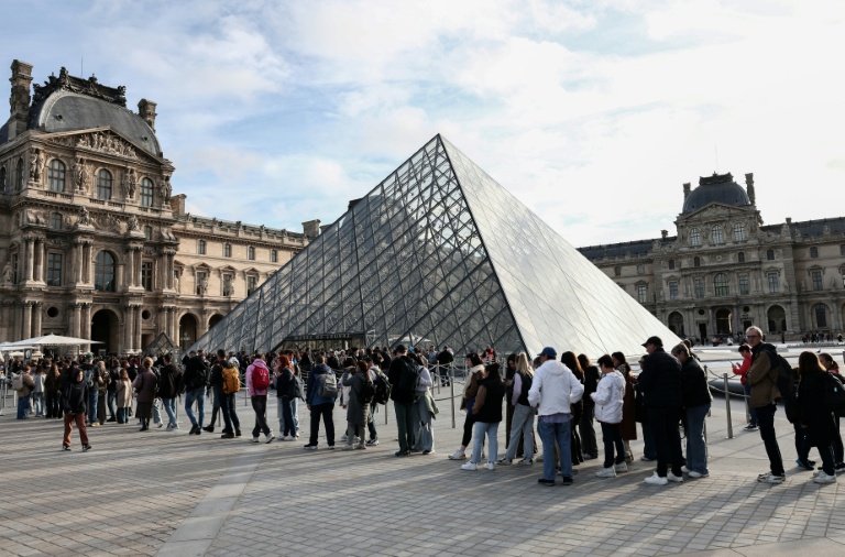 Des visiteurs font la queue devant la Pyramide du Louvre, conçue par l'architecte sino-américain Ieoh Ming Pei, et le musée du Louvre le jour de sa réouverture après un vol de bijoux, le 22 octobre 2025 à Paris