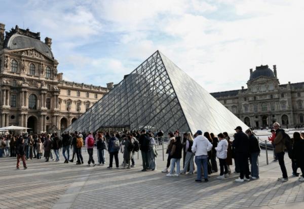 Des visiteurs font la queue devant la Pyramide du Louvre, conçue par l'architecte sino-américain Ieoh Ming Pei, et le musée du Louvre le jour de sa réouverture après un vol de bijoux, le 22 octobre 2025 à Paris